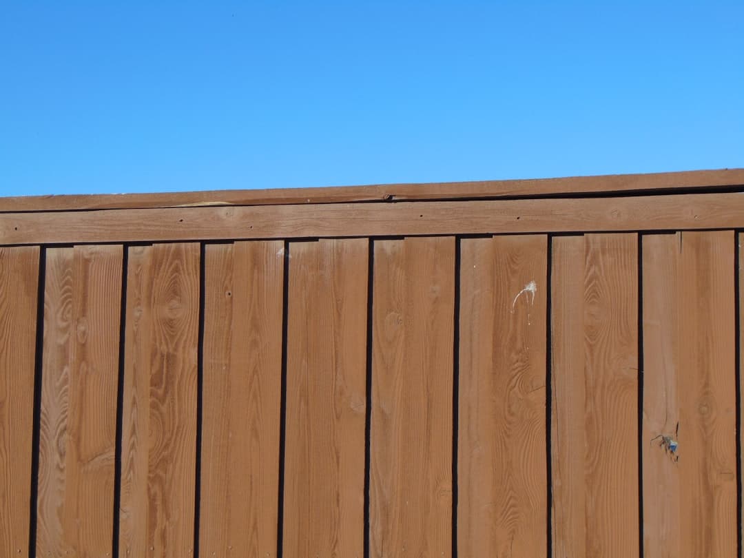A wooden garden fence with a rich brown finish against a blue sky